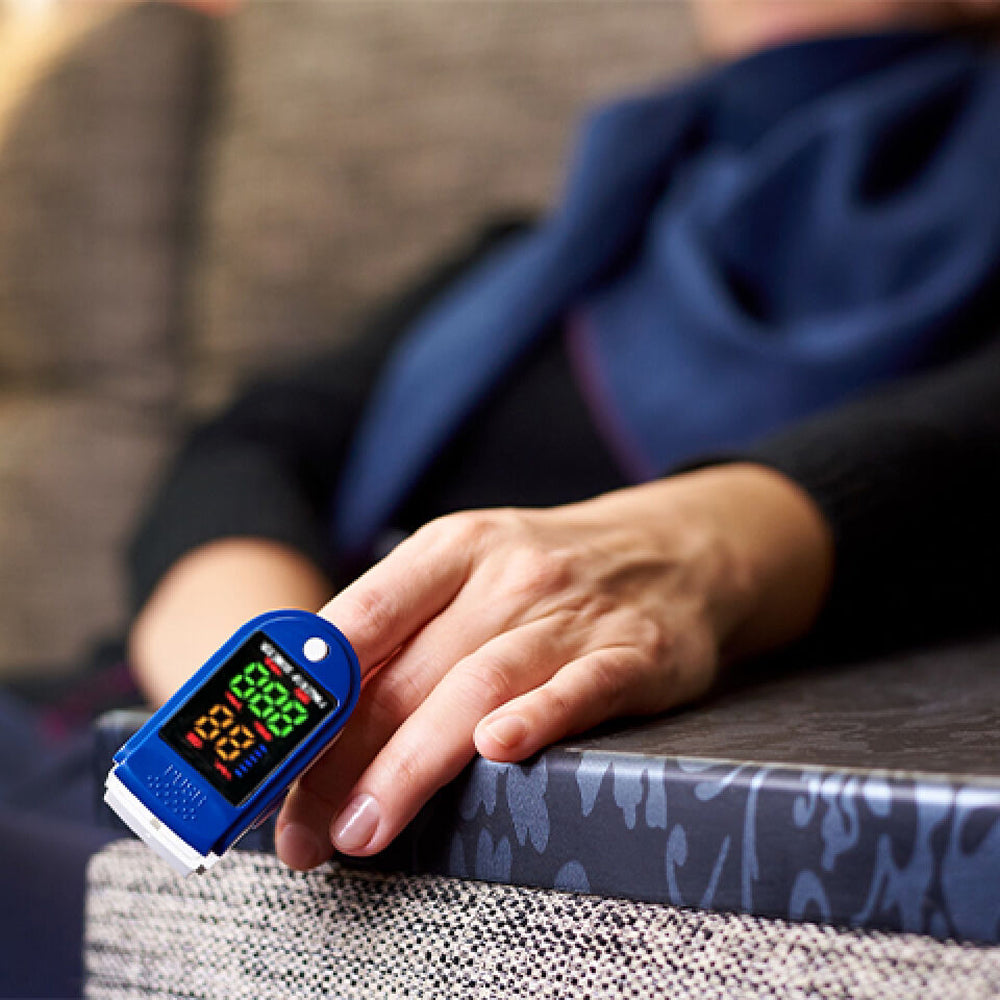 Person using a OxiLuny v2 Pulse Oximeter on their finger with a blurred background