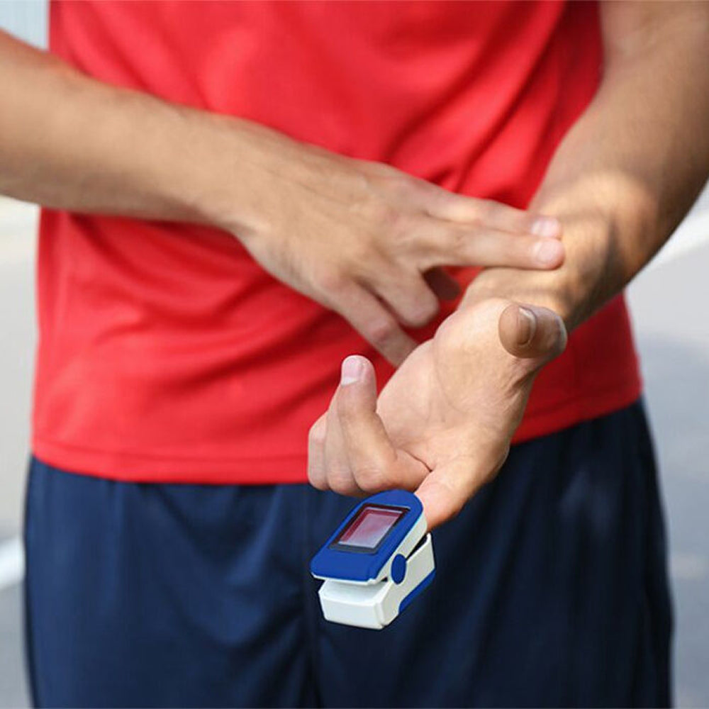 Person using a OxiLuny v2 Pulse Oximeter on their finger with a red shirt and blue shorts.