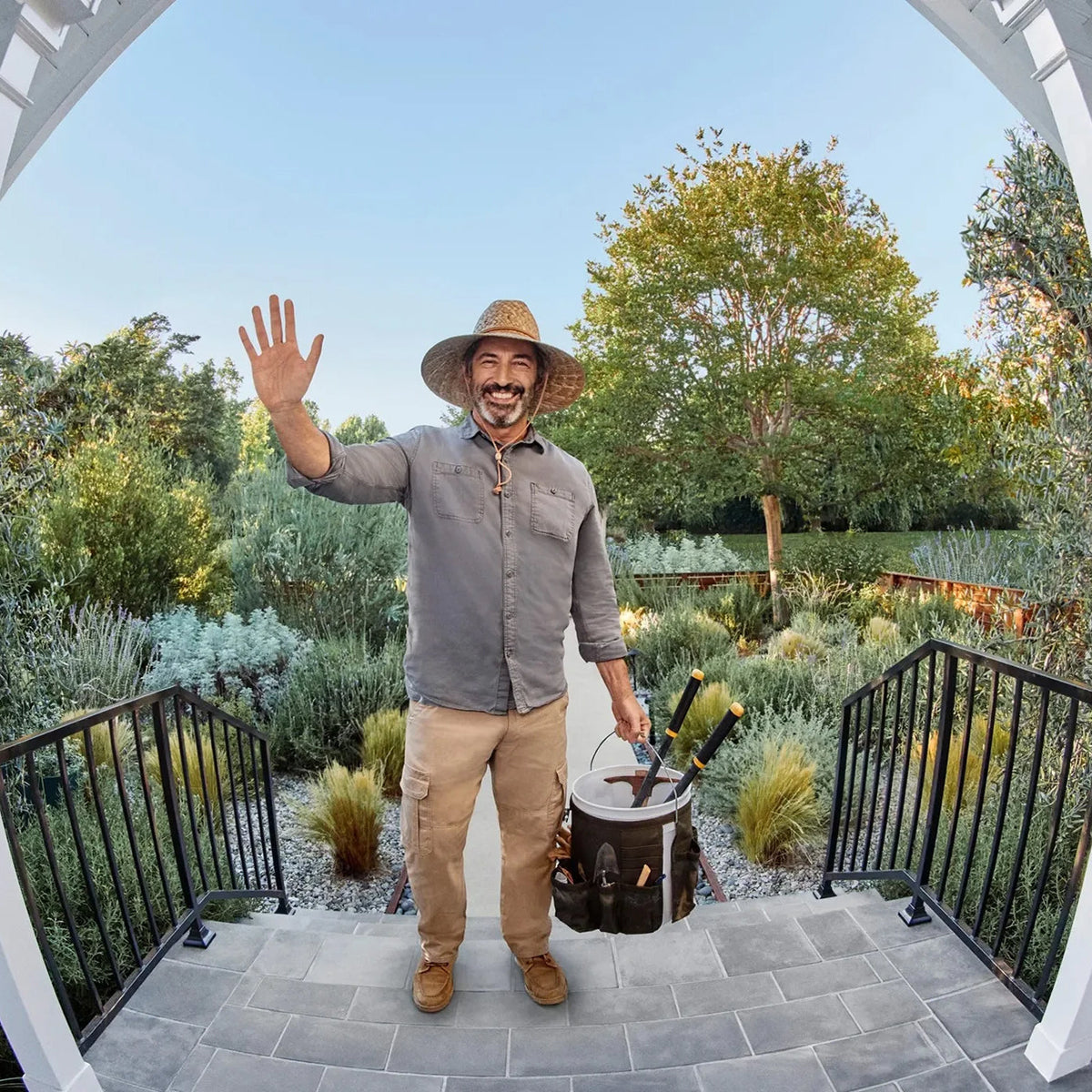 Man in a garden setting with tools, waving at the  PurePeeki Camera Doorbell 