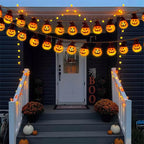 A front porch decorated for Halloween with multiple strings of Sunpikoex Solar Pumpkin Lights  draped across the entryway, white railings with warm lights, pumpkins, mums, and a vertical BOO sign on the door.