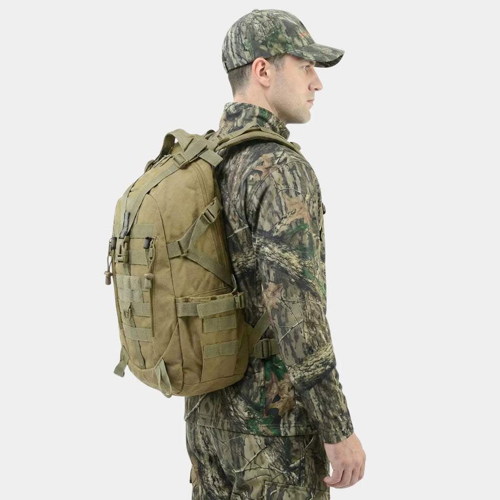 A man in a woodland camouflage outfit and cap shown from the side, wearing a The Trekorago Hunting Backpack with multiple straps and pockets against a light gray background.