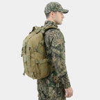 A man in a woodland camouflage outfit and cap shown from the side, wearing a The Trekorago Hunting Backpack with multiple straps and pockets against a light gray background.