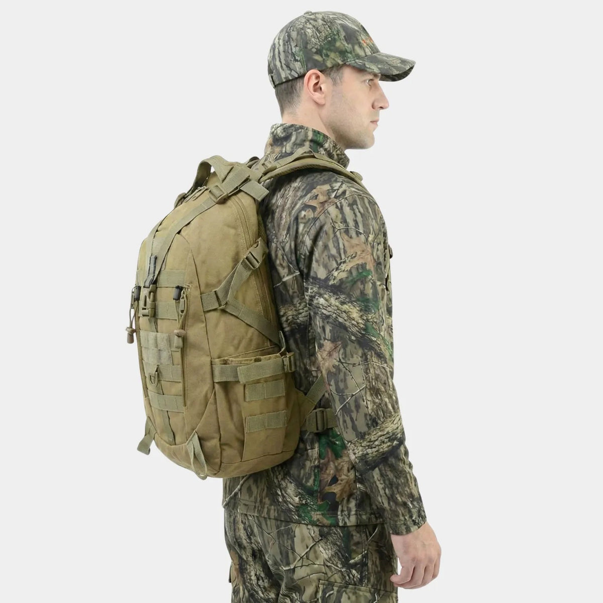 A man in a woodland camouflage outfit and cap shown from the side, wearing a The Trekorago Hunting Backpack with multiple straps and pockets against a light gray background.
